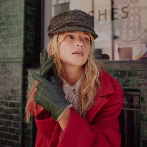 Woman stood in front of a shop, wearing dark green leather gloves with a beige knitted cuff/lining.