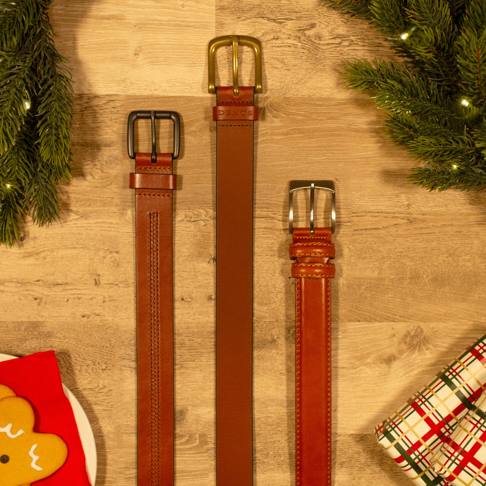 Selection of men's brown leather belts against a wooden background with Christmas accessories