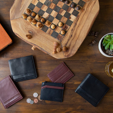 Men's various leather wallets in brown and black on a coffee table with a chessboard