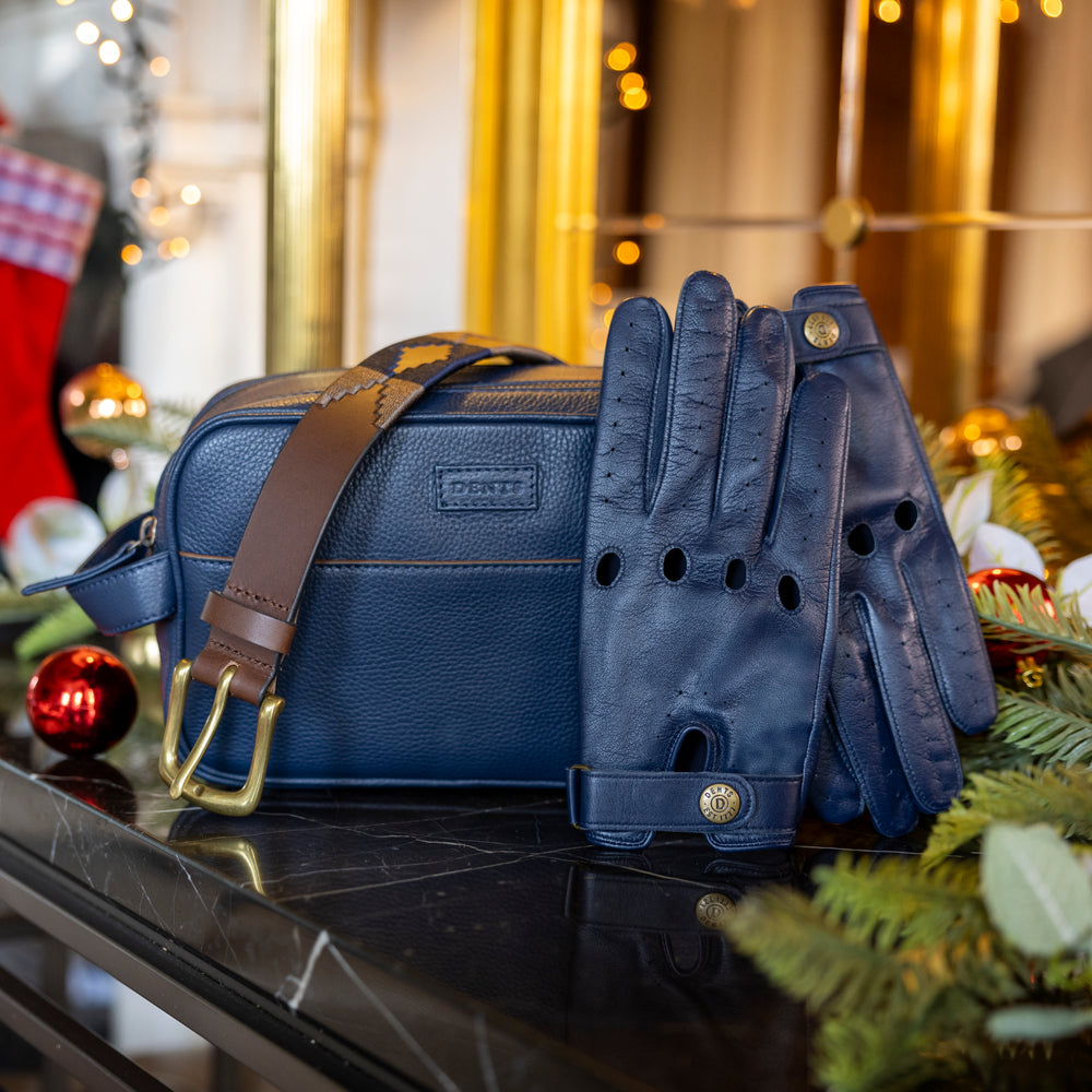 Men's Christmas gifts including navy blue leather driving gloves, a navy leather wash bag and leather polo belt with a festive background