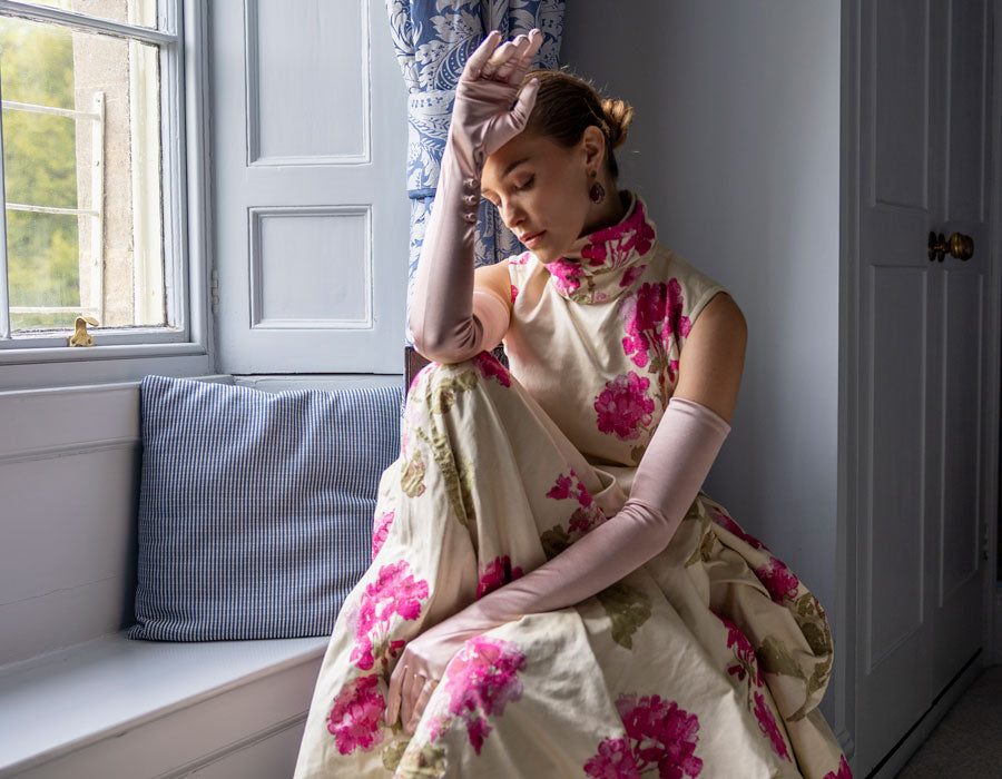 Woman wearing long evening satin gloves in rose sitting by the window