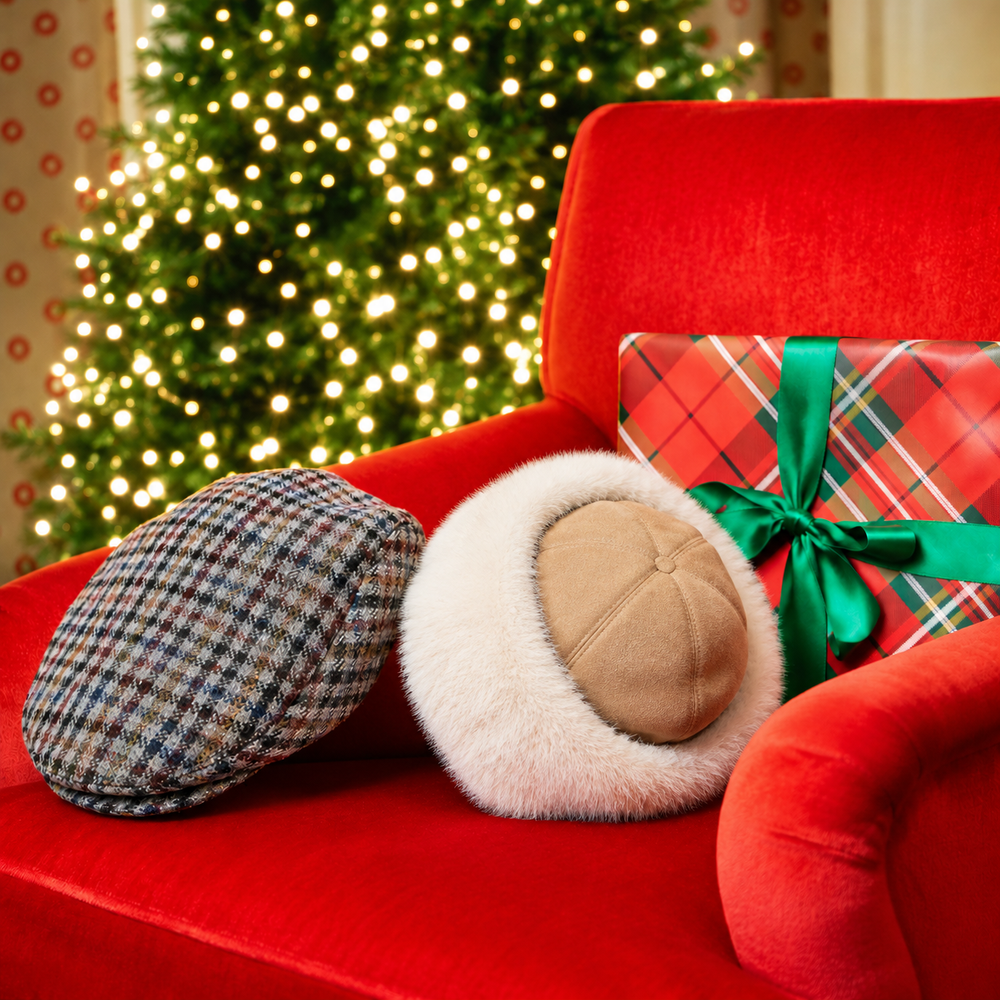 One men's tweed flat cap and a woman's faux fur-trimmed suede hat on a red armchair in front of a Christmas tree