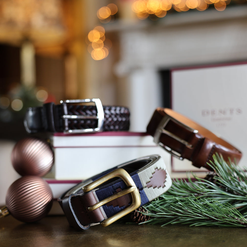 Three leather men's belts in various styles with Christmas baubles and green foliage on a table with a festive background