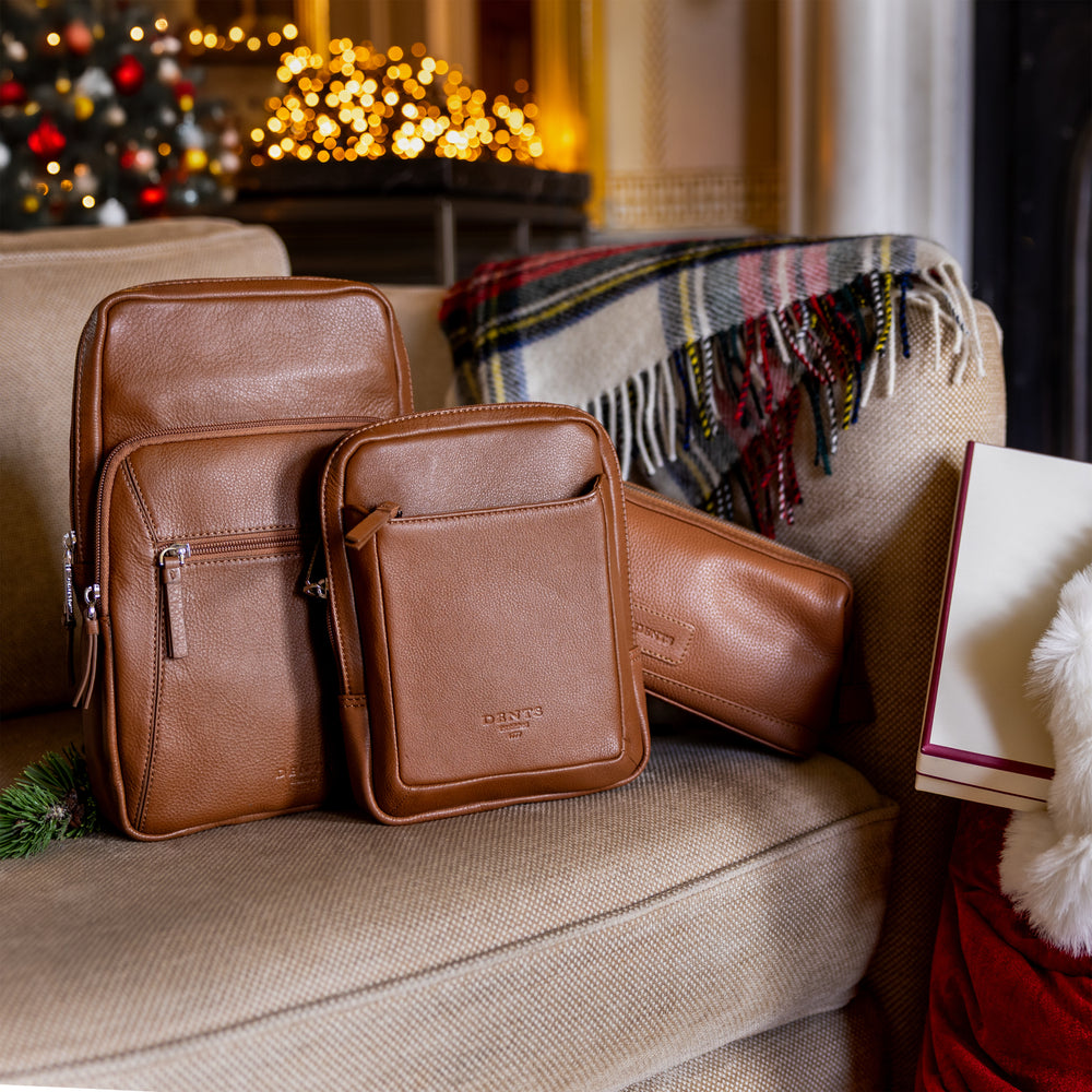 Four men's brown leather bags with a checked cashmere throw on a cream sofa in front of a festive background