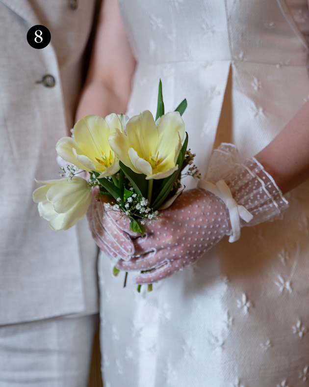 Close up of woman wearing spotty tulle gloves with double cuff and bow in ivory while holding flowers.