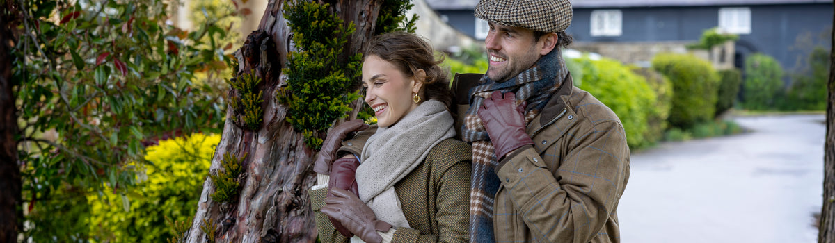Man and woman wearing brown leather gloves with scarves and hats outdoors