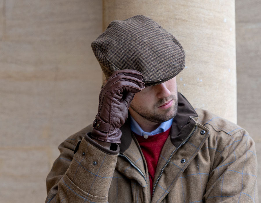 Man wearing a tweed flat cap in brown colour outdoors with leather gloves