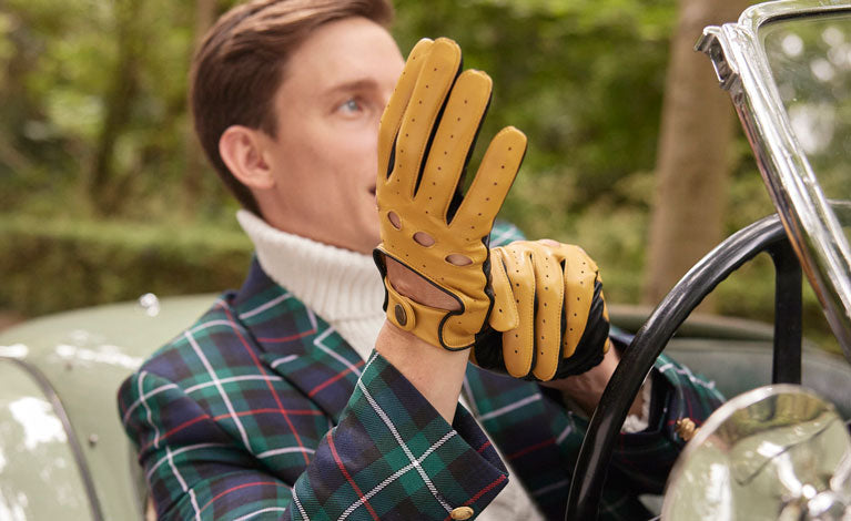 Man wearing leather driving gloves in cork/black sitting behind the wheel of a classic car