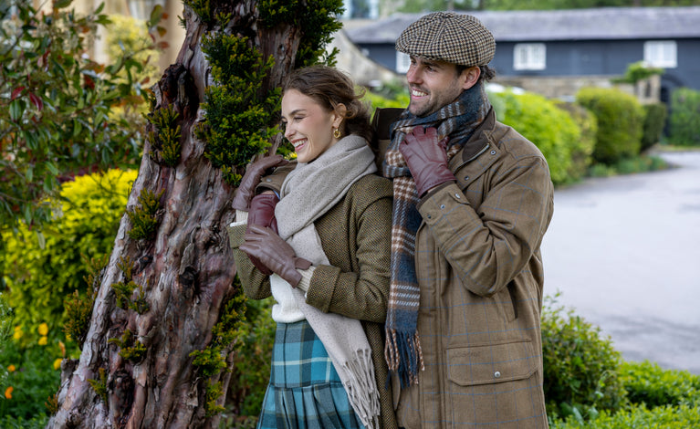 Man and woman wearing brown leather gloves with scarves and hats outdoors