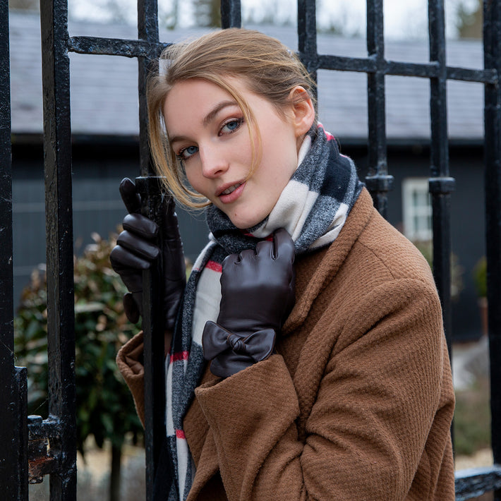 Woman wearing leather gloves with a bow and a checked scarf by a metal gate